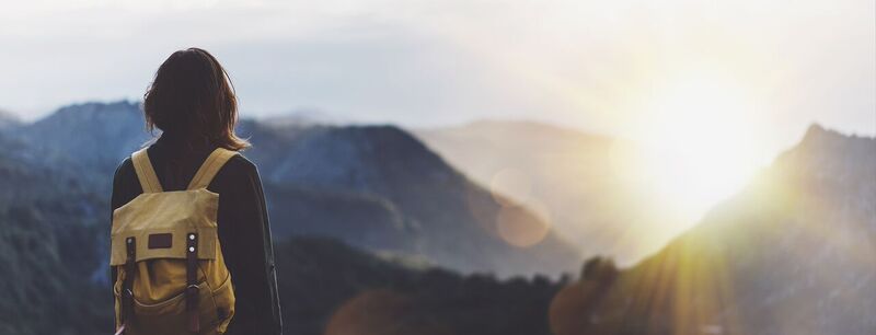 Una mujer de espaldas mirando al horizonte con un paisaje de montañas